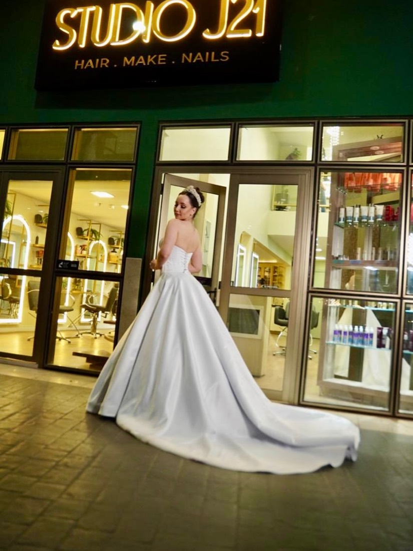 Noiva em vestido de baile na porta do Studio J21, com o letreiro do salão ao fundo