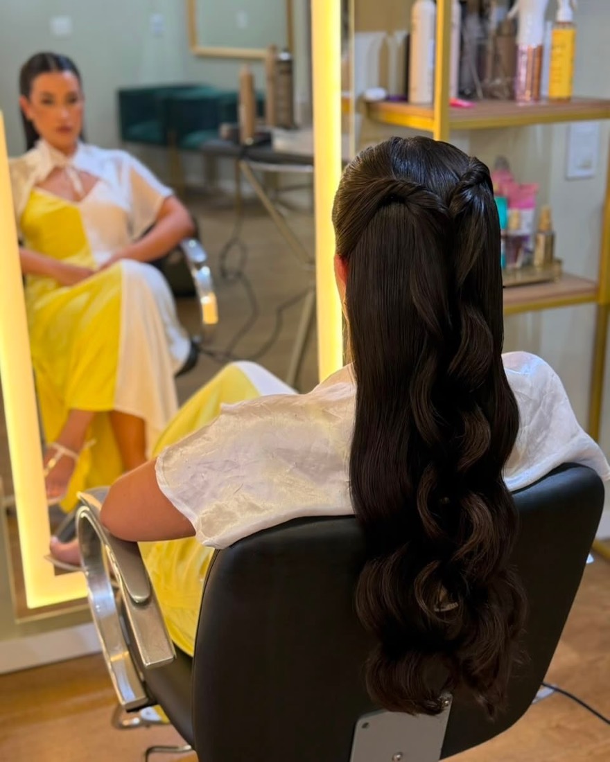 Cliente sendo penteada no salão, com o reflexo de outra cliente no espelho ao fundo